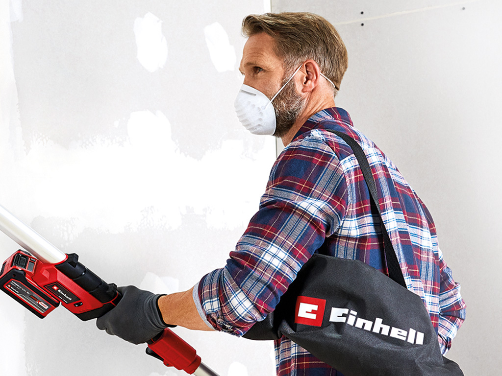 A man sands the wall with a protective mask