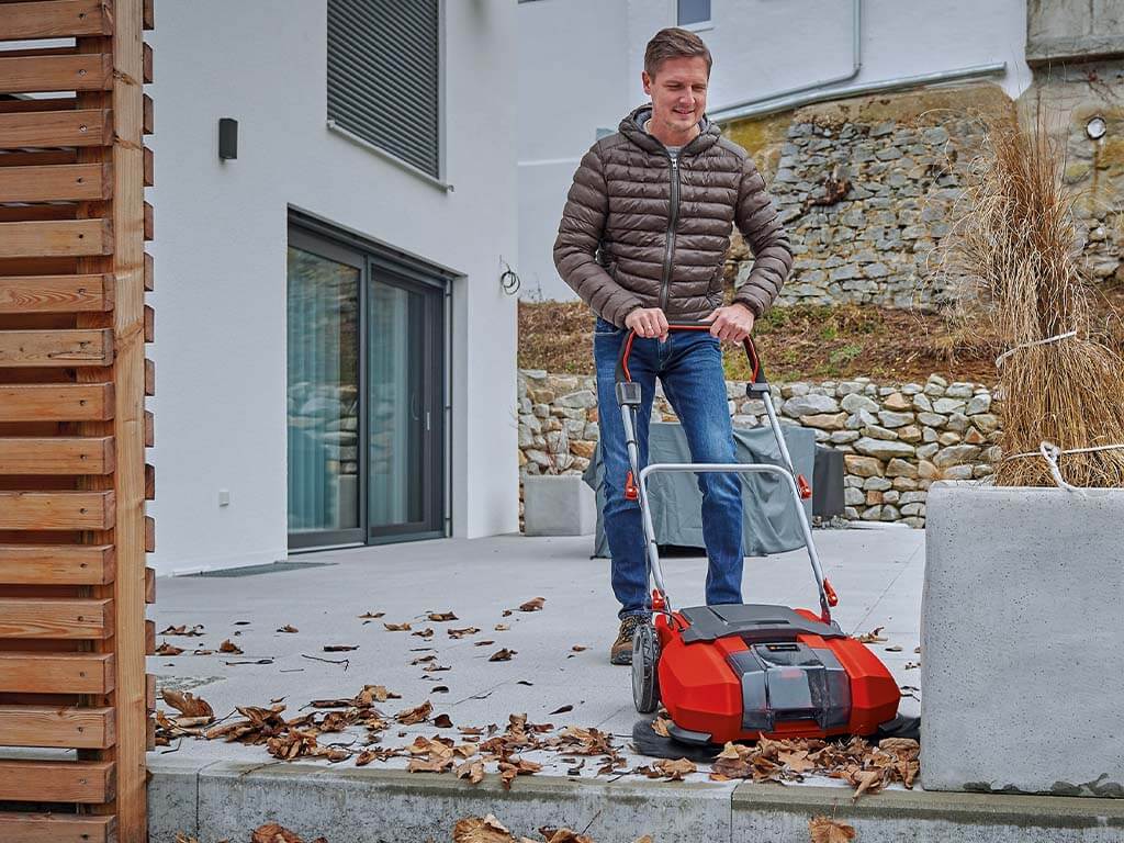 man sweeps the leaves off the terrace with a sweeper