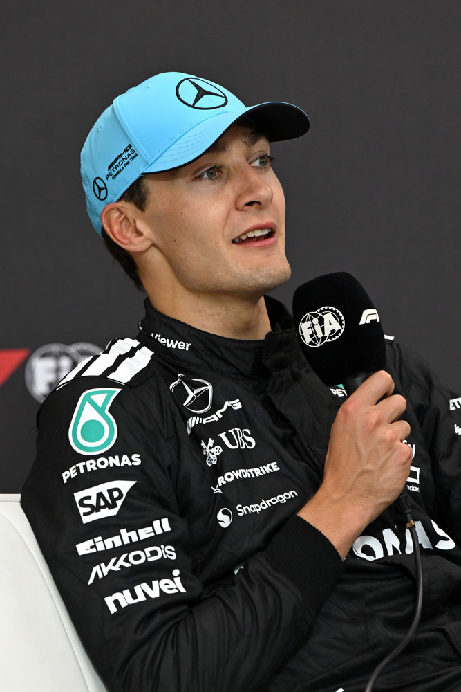 Jazdec Formuly 1 George Russell s mikrofónom v pravej ruke.