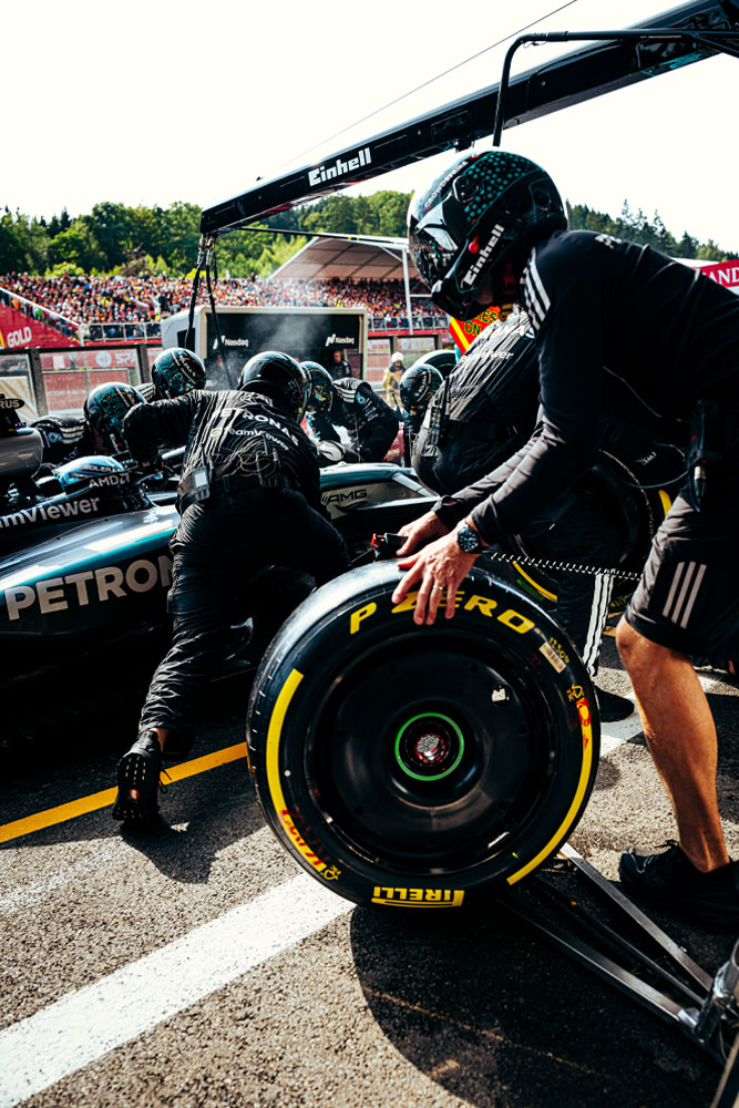 Mechanici týmu Mercedes-AMG PETRONAS Formula One Team provádějí zastávku v boxech. Jeden člen připravuje pneumatiku Pirelli, zatímco ostatní pracují na voze. Logo Einhell je viditelné na vybavení nad vozem.