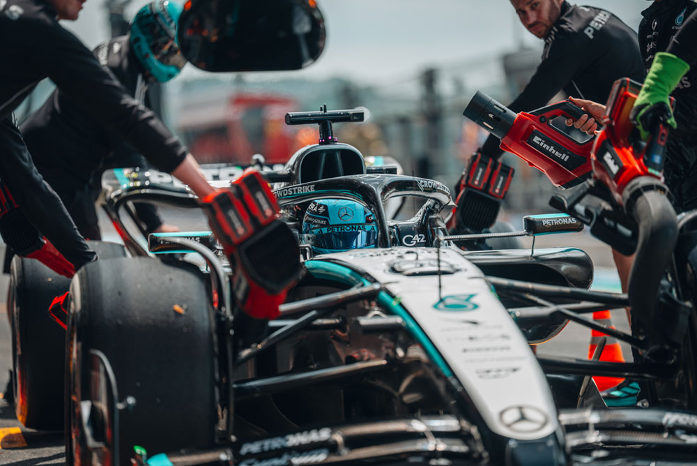 Vůz Mercedes-AMG PETRONAS Formula One Team během zastávky v boxech. Členové týmu používají bezdrátové foukače Einhell k ochlazení komponentů vozidla. Tým je soustředěný a pracuje s přesností.