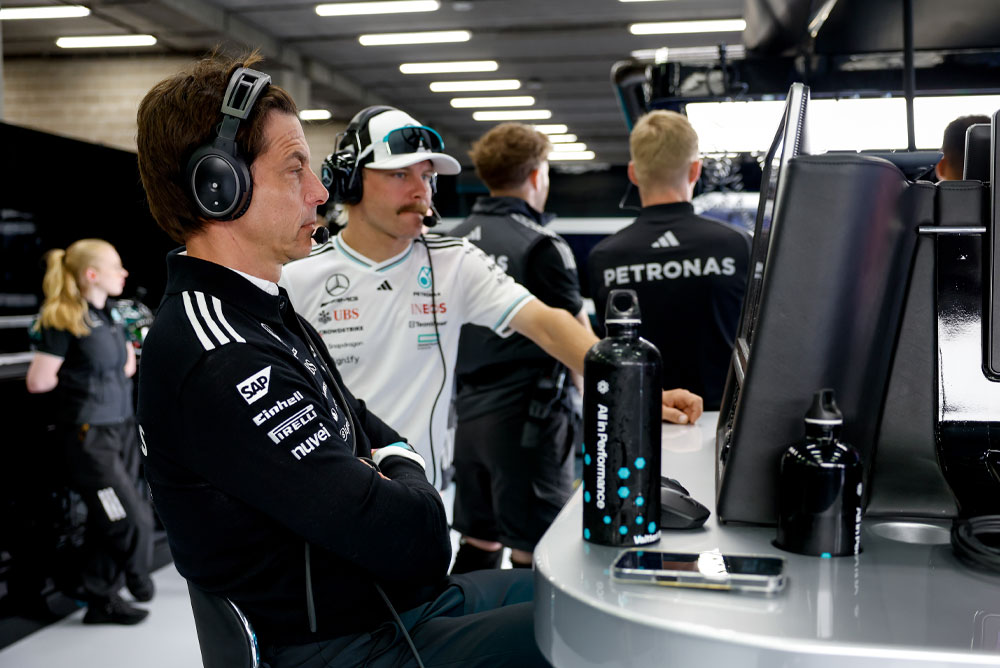Toto Wolff a Valtteri Bottas z týmu Mercedes-AMG PETRONAS Formula One Team jsou vidět na týmovém pracovním stanovišti v garáži. Soustředí se na závodní strategii, sledují monitory a komunikují prostřednictvím sluchátek.