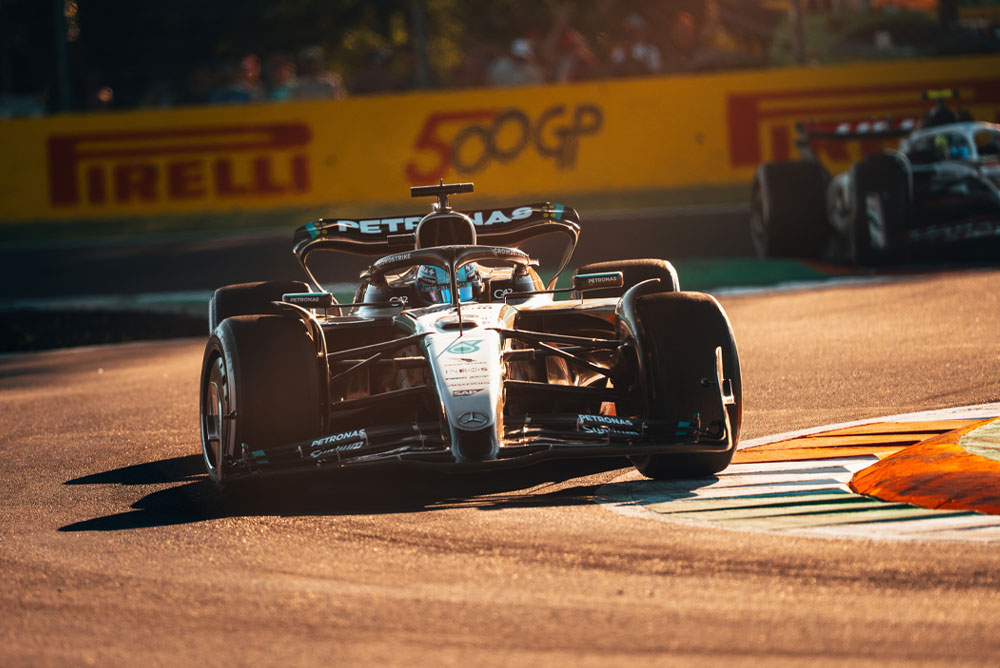 Vůz Mercedes-AMG PETRONAS Formula One Team jede po sluncem zalité trati během Velké ceny. Auto projíždí zatáčkou vysokou rychlostí, zatímco v pozadí je vidět další vůz.