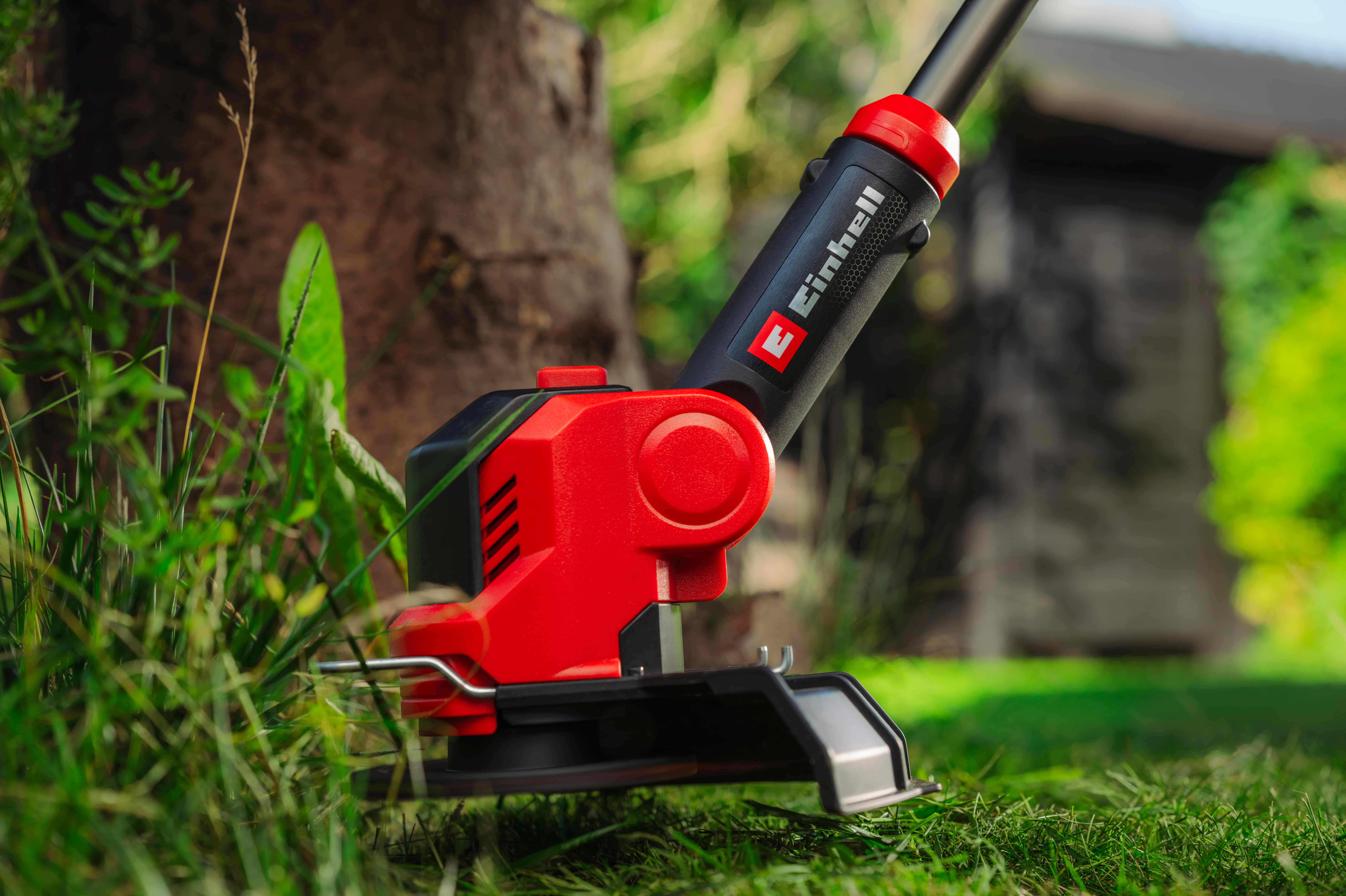 Einhell vyžínač kosí trávu okolo stromu v záhrade.