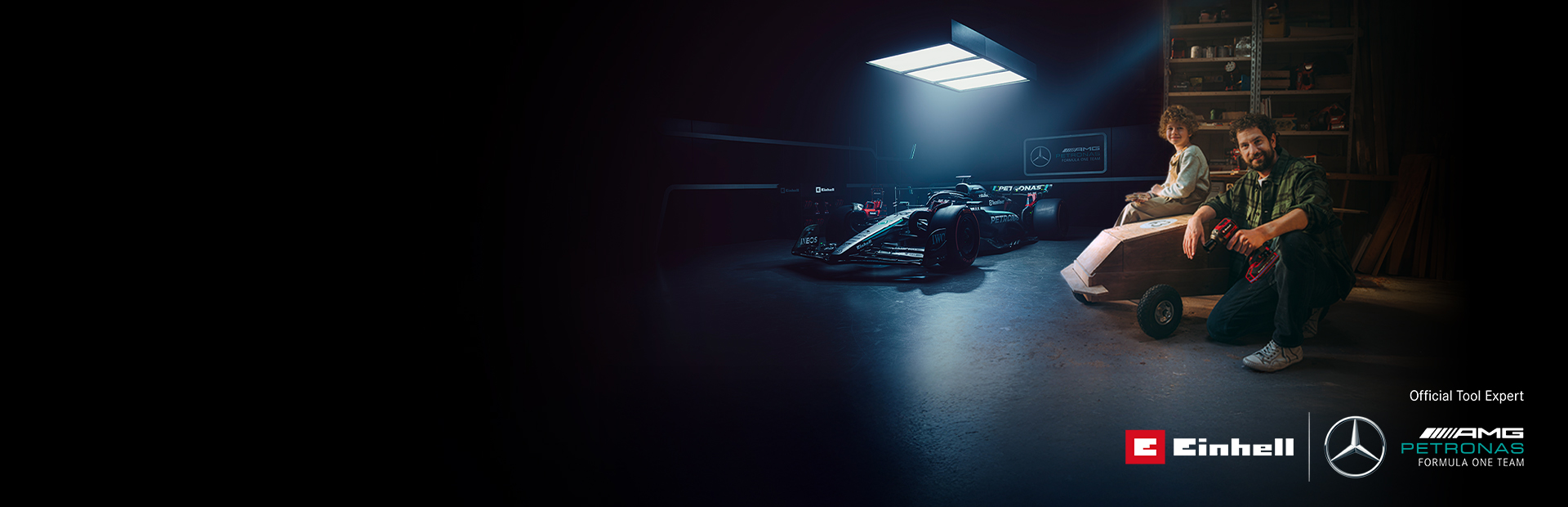 Otec a dieťa sú v dielni s doma vyrobeným vozíkom (soapbox). V pozadí je auto Formuly 1 Mercedes-AMG PETRONAS a náradie Einhell.