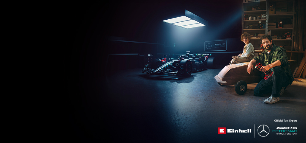 Otec a dieťa sú v dielni s doma vyrobeným vozíkom (soapbox). V pozadí je auto Formuly 1 Mercedes-AMG PETRONAS a náradie Einhell.