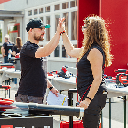 Muž a žena si dávají „high-five“ na akci Einhell pod širým nebem s výstavou nářadí, barevná fotografie.