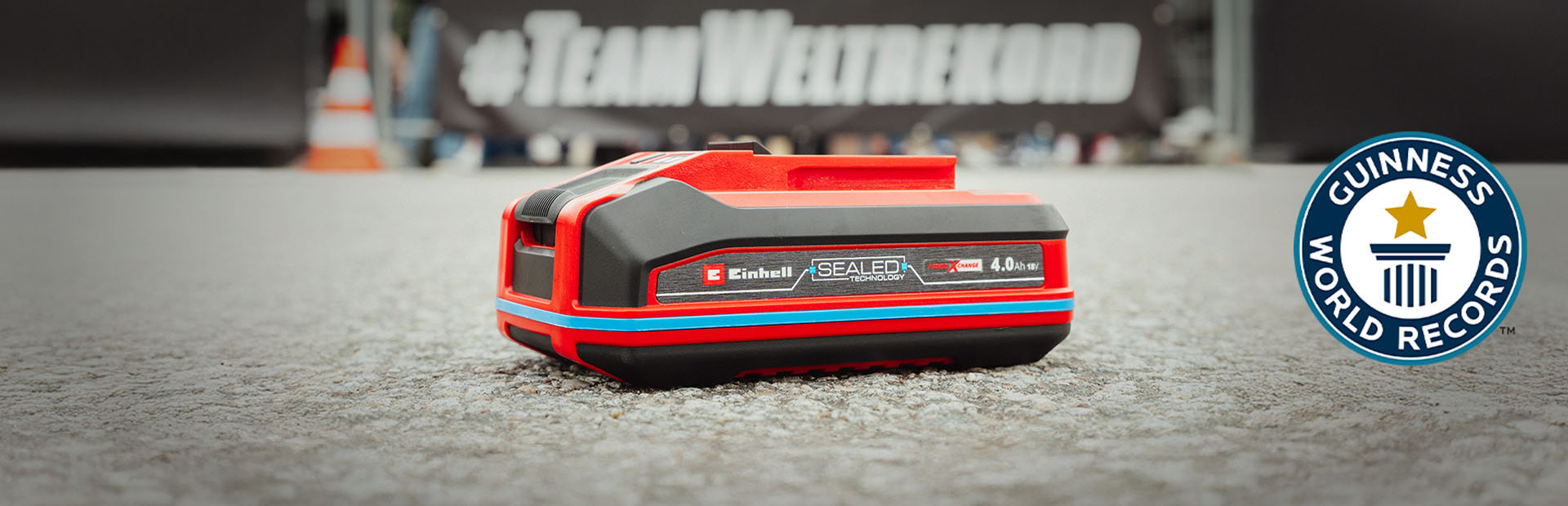 Akumulátor Einhell SEALED Power X-Change 4,0 Ah leží na asfaltu, vpravo logo Guinness World Records „Record Holder“.