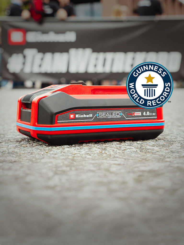 Akumulátor Einhell SEALED Power X-Change 4,0 Ah leží na asfaltu, vpravo logo Guinness World Records „Record Holder“.