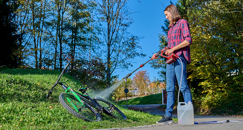 a woman is cleaning a bicycle with the Einhell cordless high pressure cleaner HYPRESSO