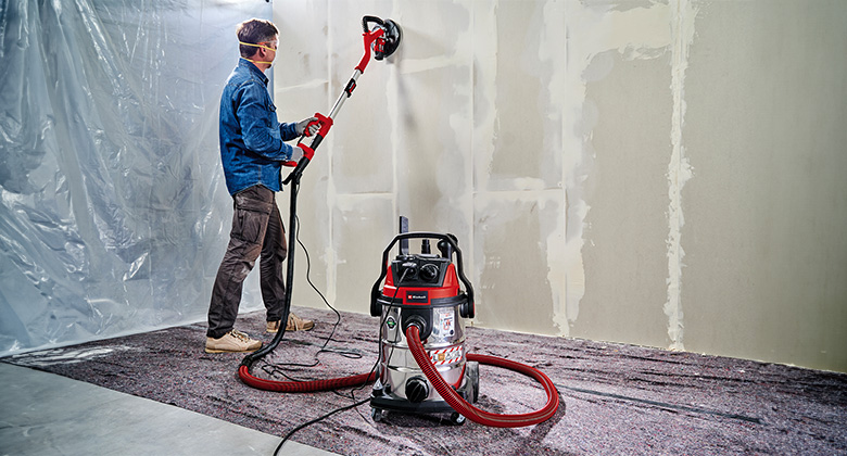A man uses an Einhell wet/dry vacuum to extract dust during drywall construction work